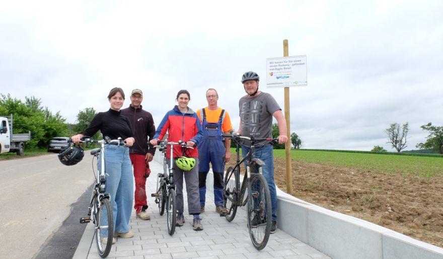 Vorher: Die Alte Poststraße am Ortsausgang ohne Radweg, Nachher: Jana Stahl (Energieagentur Südwest), Matthias Änis (Fa. Matthias und Markus Änis Gbr, Rümmingen), Olivia Howe (Energieagentur Südwest), Werner Sturm (Werkhof Vorderes Kandertal) und Chrisitan Iselin (Bürgermeister Schallbach) (v.l.) freuen sich über ein neues Stück sicherer Radweg; Foto: Energieagentur Südwest